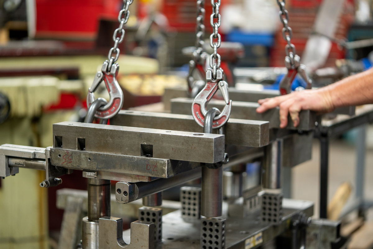 Mechanical custom metal stamping press tooling, hoisted by a crane in the tool shop for maintenance work.